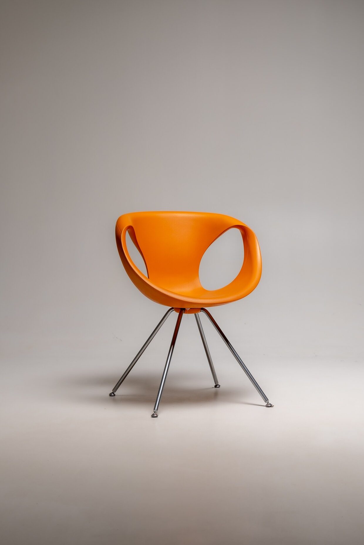 Oranger Designstuhl aus Kunststoff mit schlanken Metallbeinen freigestellt vor neutralem Hintergrund im Fotostudio