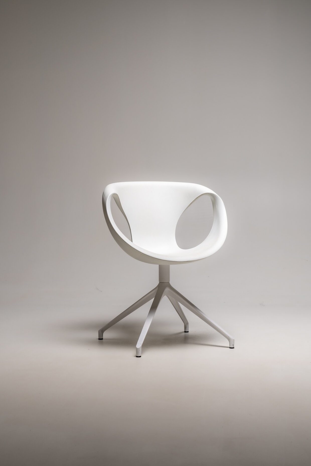 Weißer moderner Designstuhl mit organischer Form und vierarmigem Drehfuß vor hellem Studiohintergrund