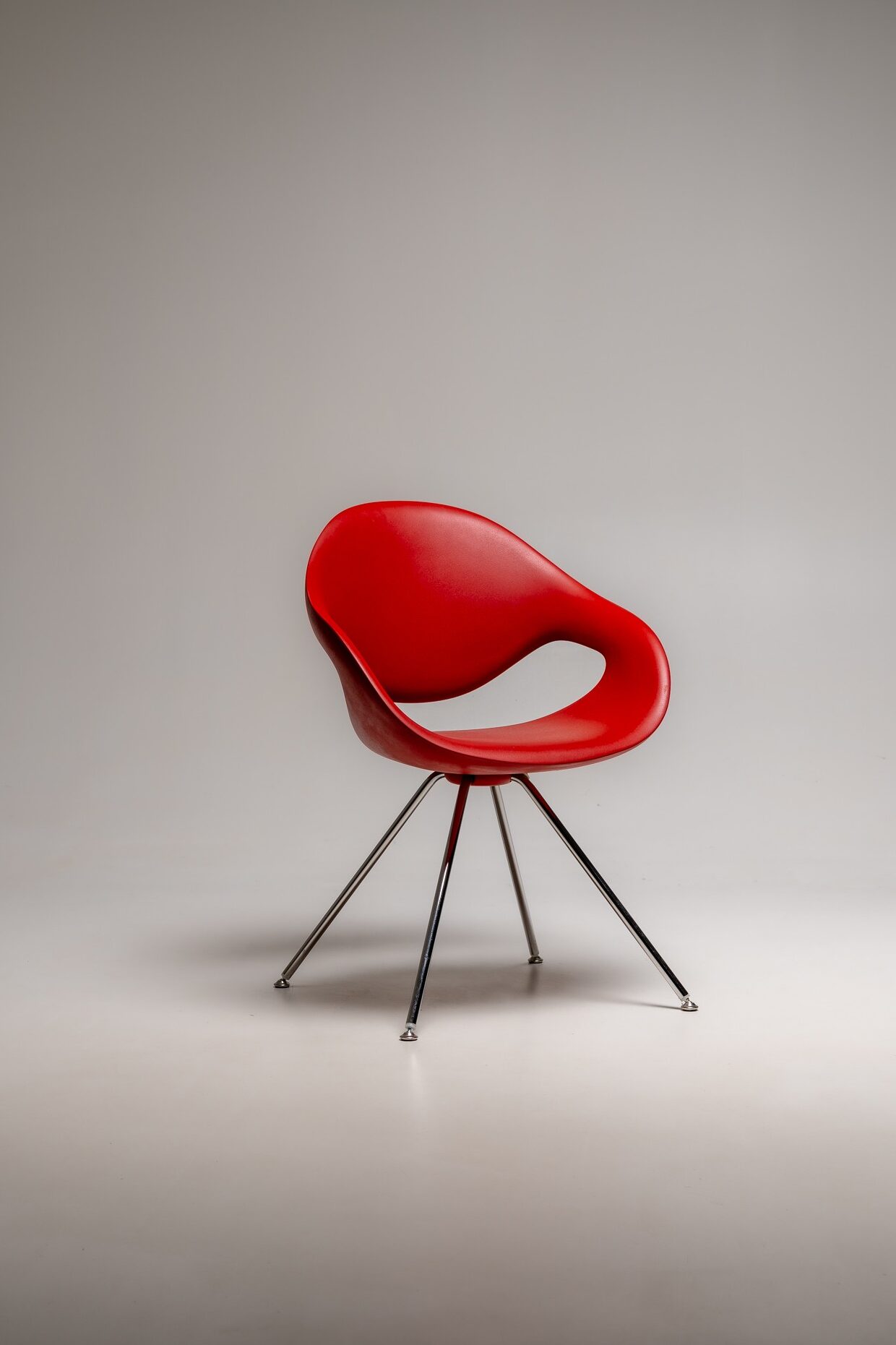 Roter moderner Designstuhl mit geschwungener Sitzfläche und Metallbeinen vor neutralem Studiohintergrund