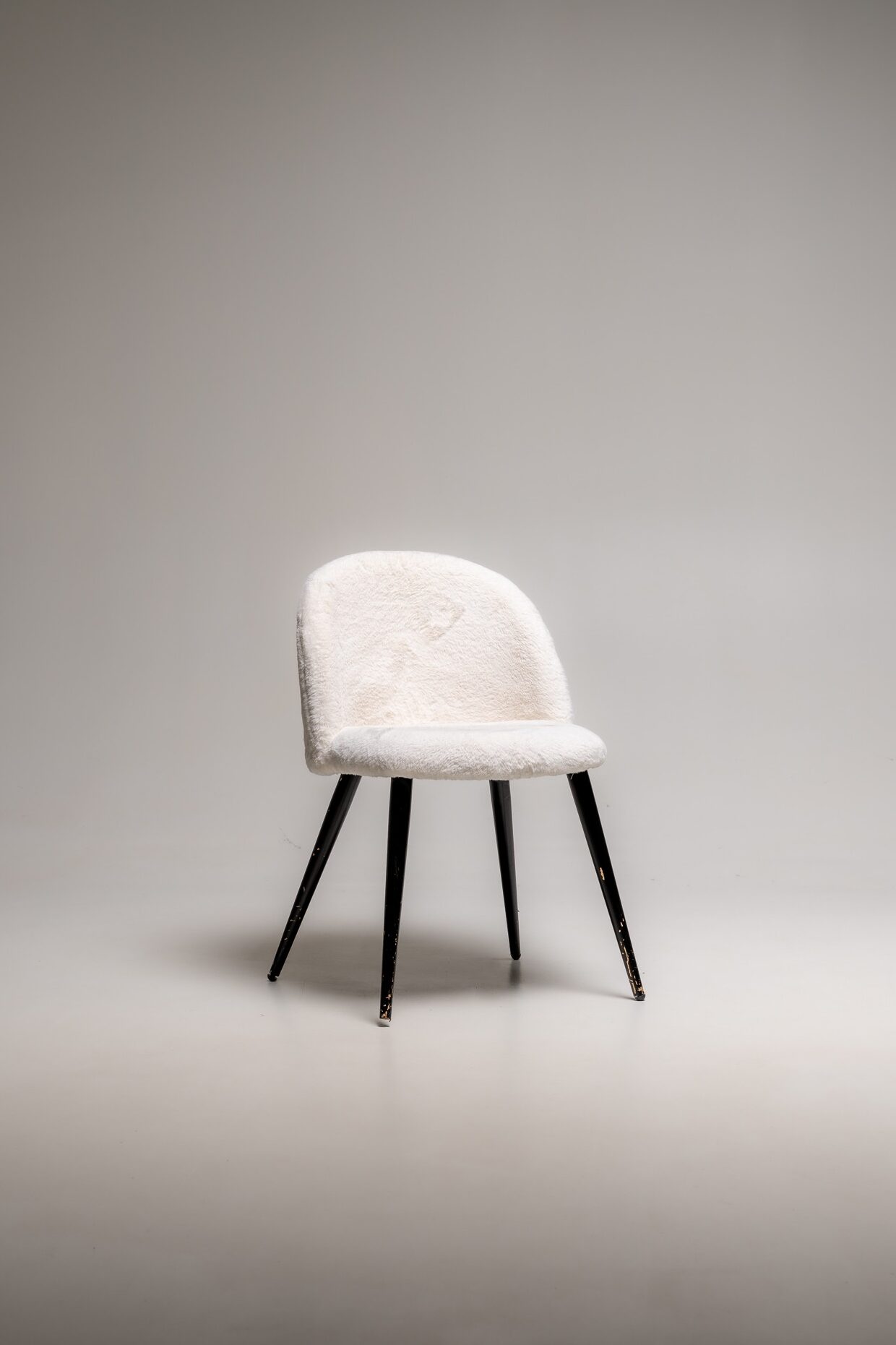 Gepolsterter Stuhl mit weißem Bouclé-Stoff und schwarzen Holzbeinen freigestellt im Fotostudio