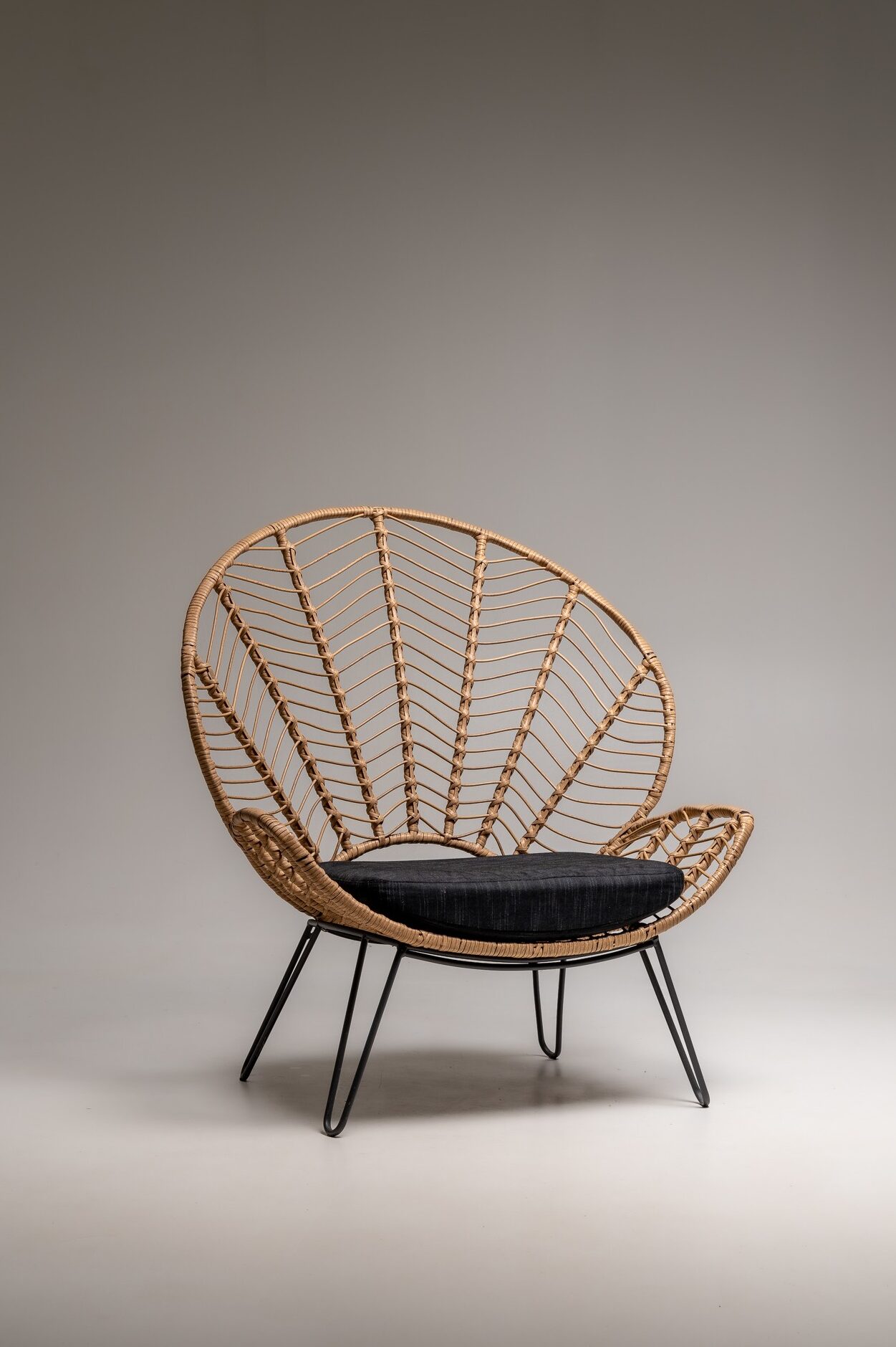 Loungesessel aus Rattan mit schwarzem Sitzkissen und Metallbeinen freigestellt vor neutralem Studiohintergrund