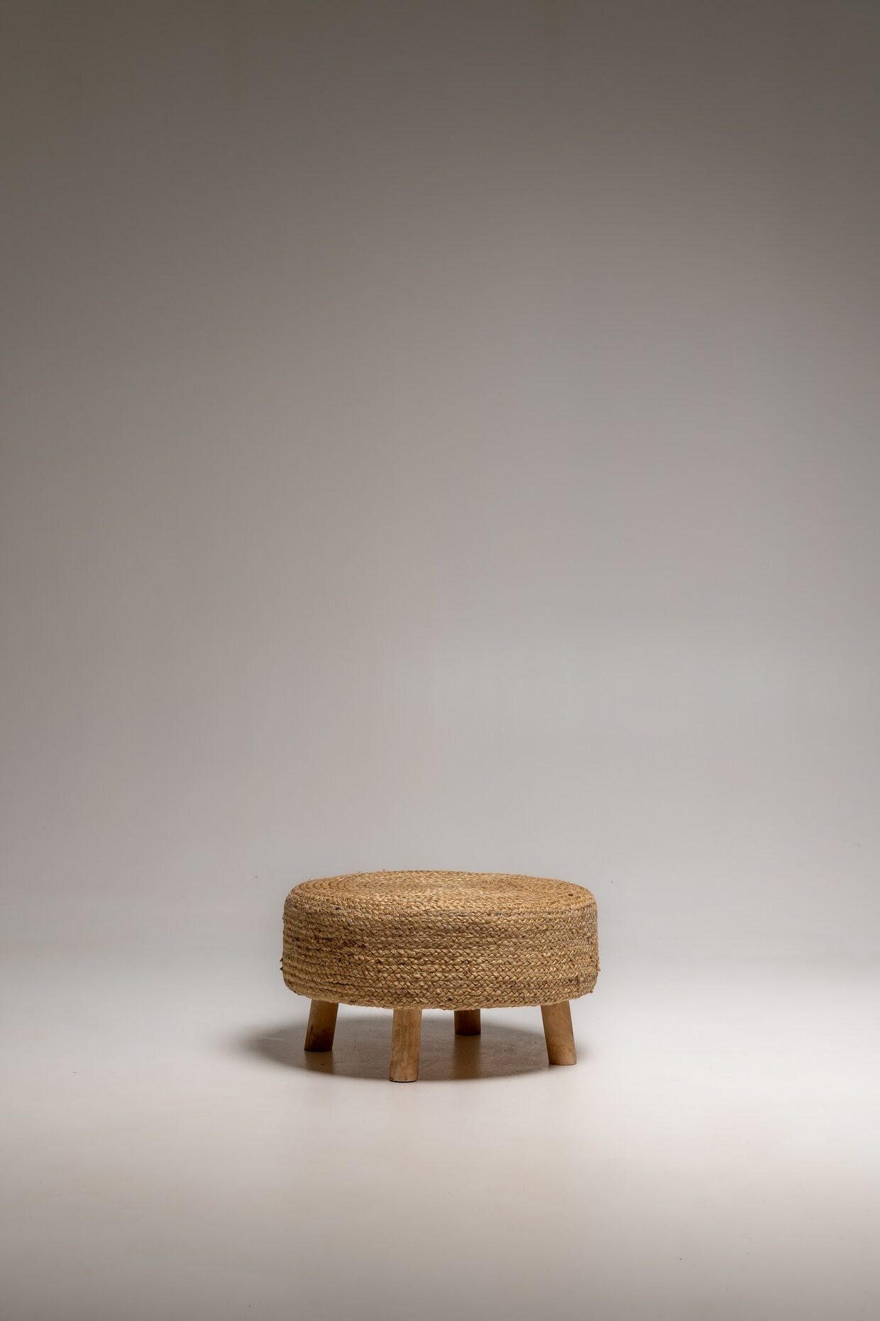 Niedriger runder Hocker aus geflochtenem Naturmaterial mit Holzfüßen freigestellt im Fotostudio