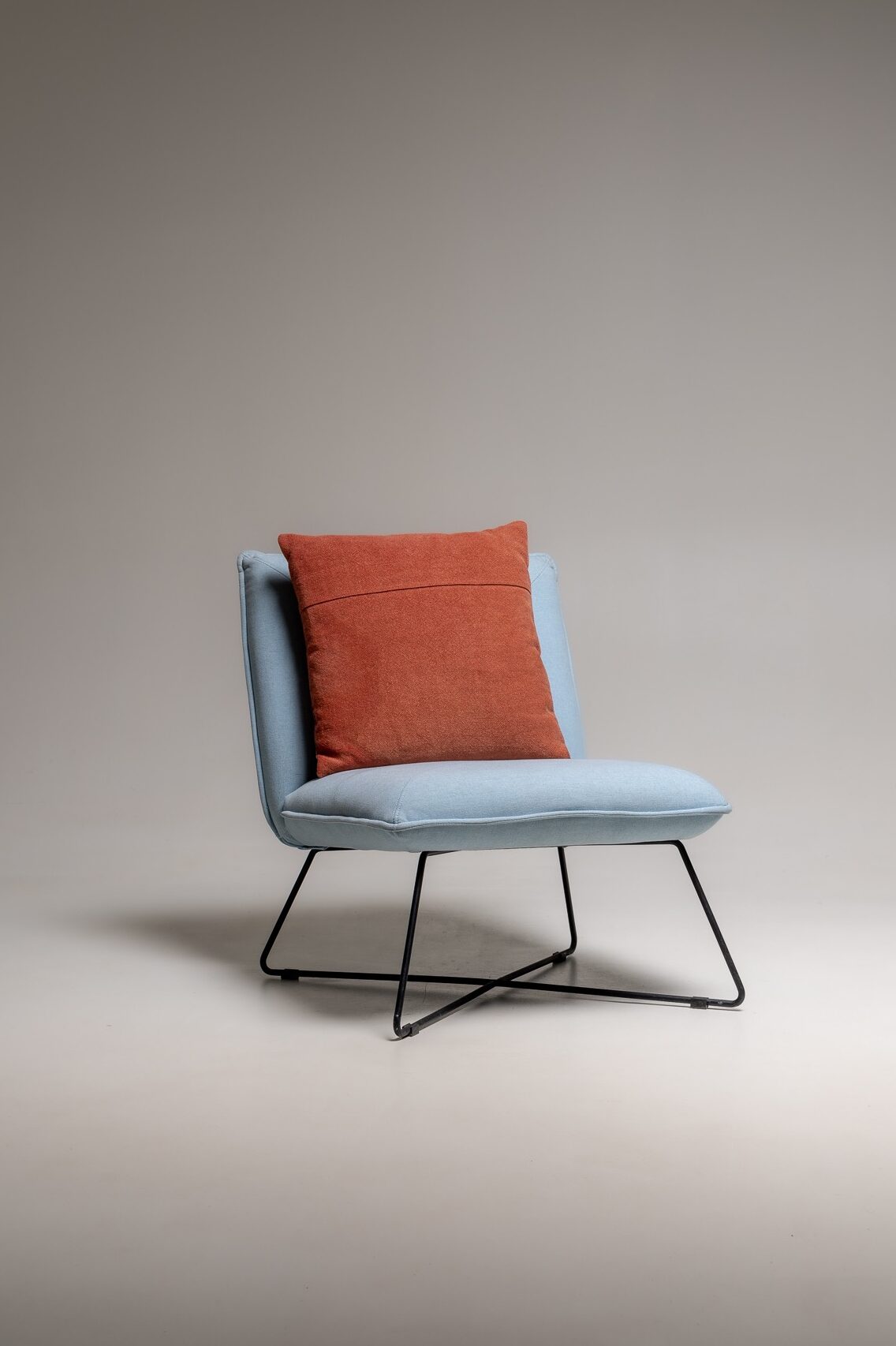 Moderner Loungesessel in Hellblau mit rostfarbenem Kissen und Metallgestell freigestellt im Fotostudio